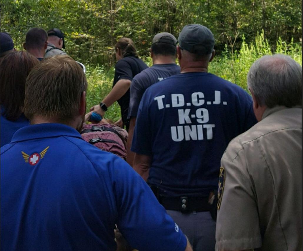 Photo of SJSO deputies, MCSO deputies, TDCJ canine handlers and Allegiance Mobile Health Services staff carrying Ms. Field in a stretcher through the woods.